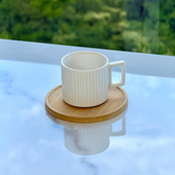 Xicara de porcelana com alca quadrada e pires de madeira refletindo em superficie marmore