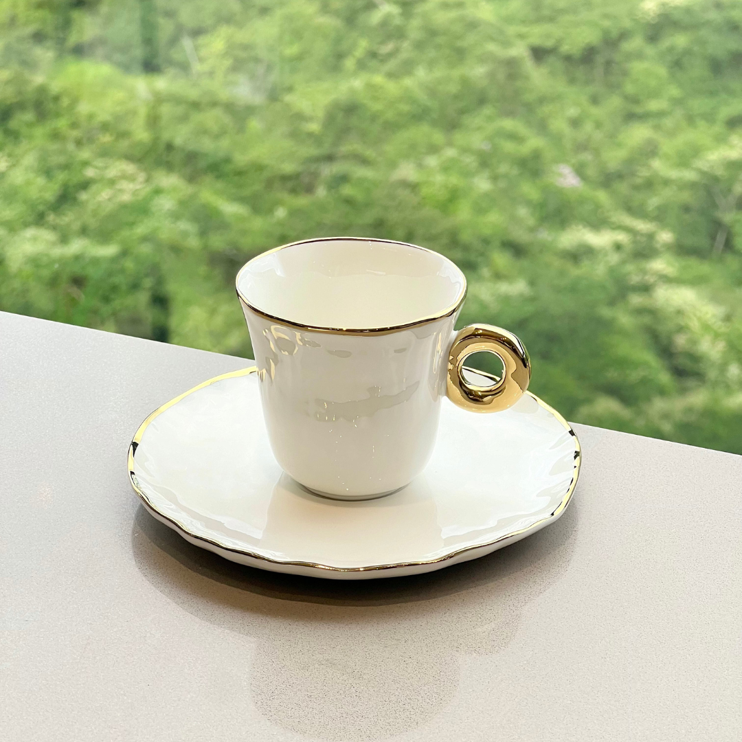 Xícara de café com pires branco e acabamento dourado em ambiente externo