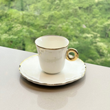 Xícara de café com pires branco e acabamento dourado em ambiente externo