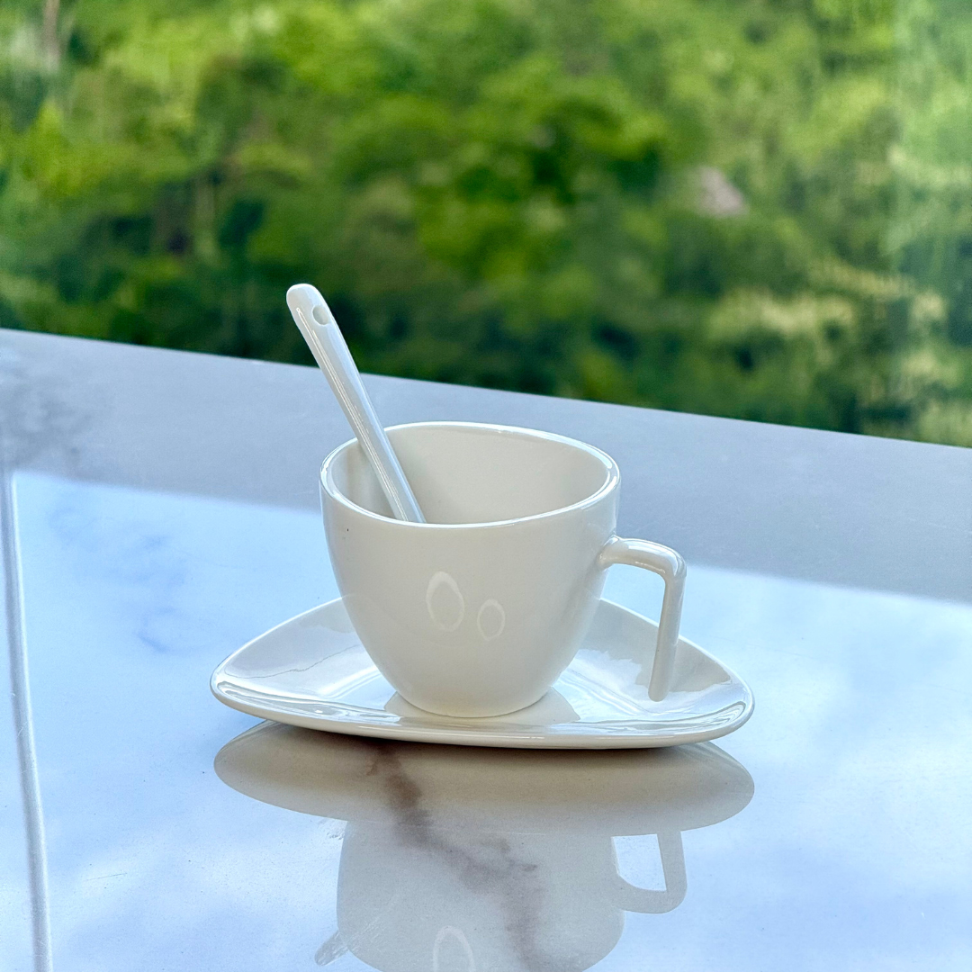 Xicara de cafe com pires triangular e colher apoiada em superficie de marmore