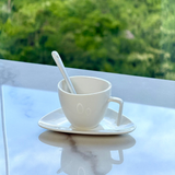 Xicara de cafe com pires triangular e colher apoiada em superficie de marmore