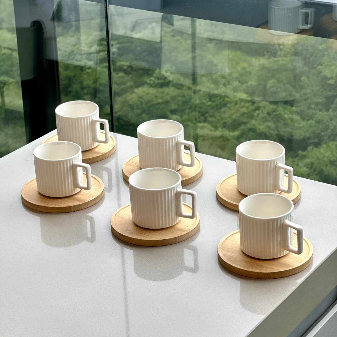 Seis xicaras de cafe em porcelana branca com pires de madeira sobre bancada branca