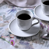 Xícara de chá branca com café servido em mesa com toalha florida