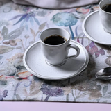 xícara de café branca com pires em mesa com toalha floral